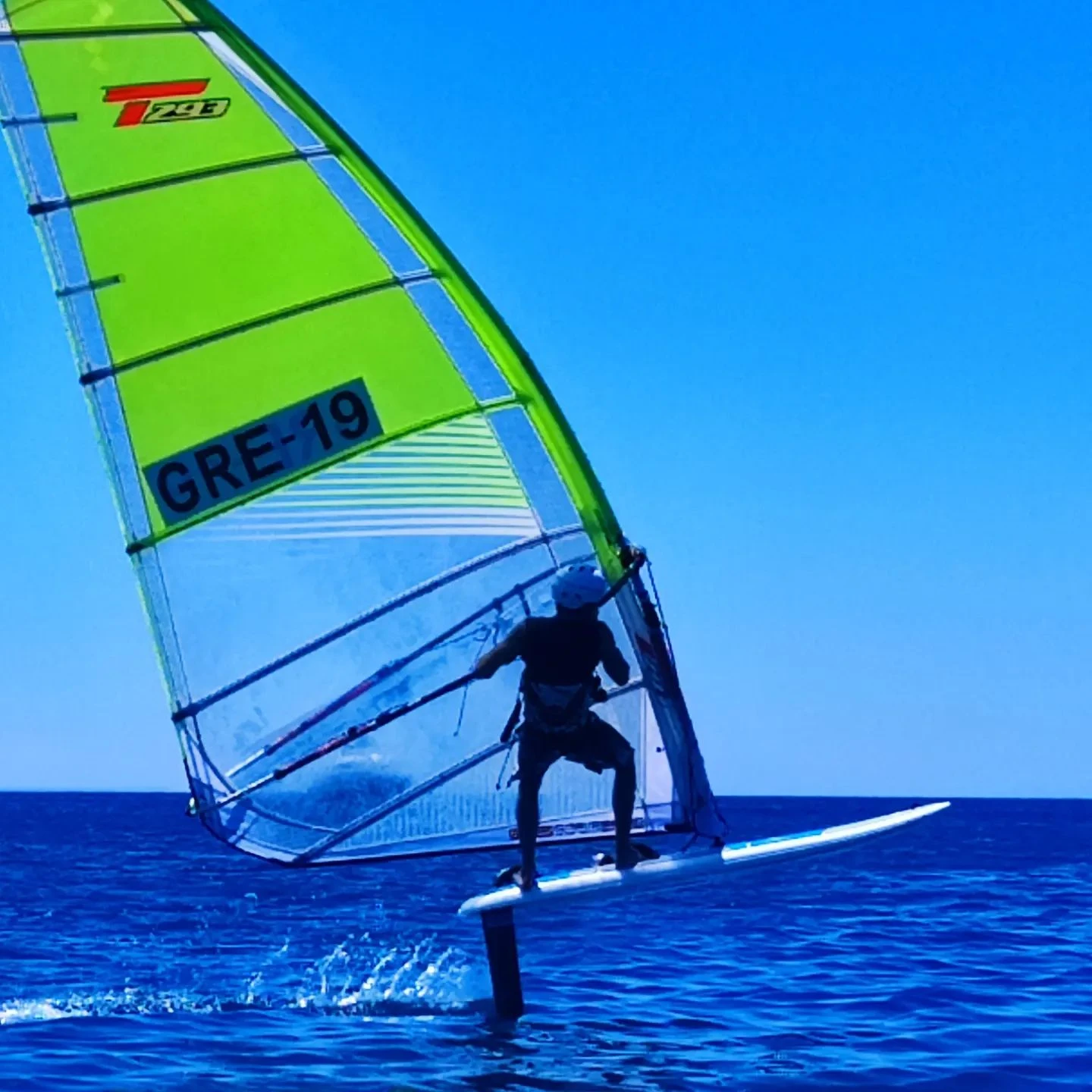 Windsurfer sailing with a green sail on open water