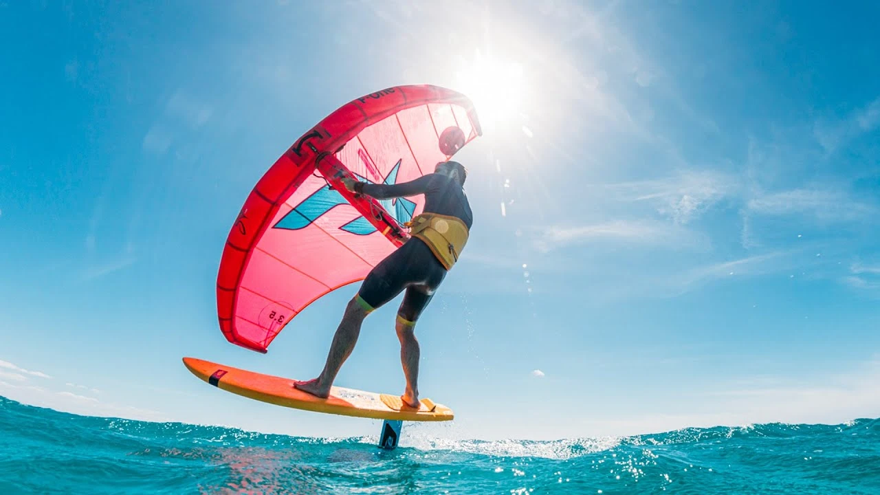 Wingfoil rider lifting above the water with a pink wing